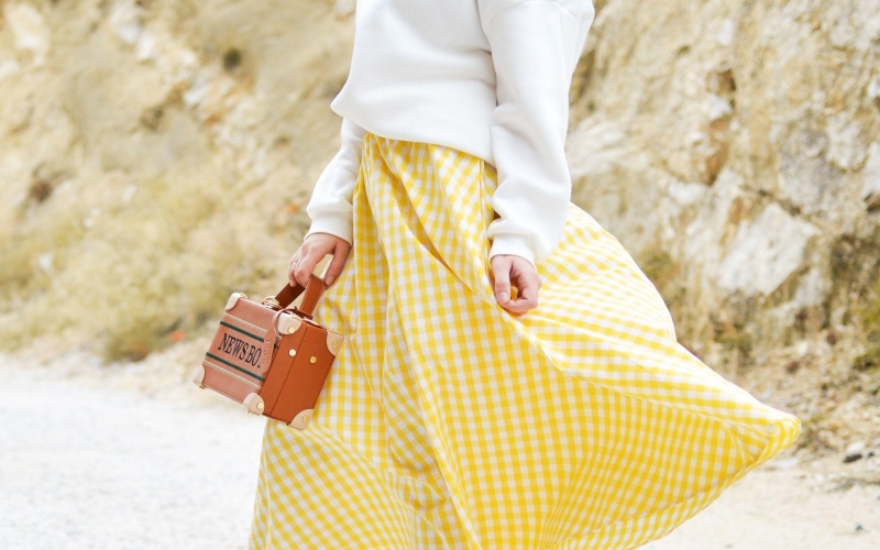 A picture of a woman wearing a checkerboard print skirt, white sweater top and carrying a fashionable handbag. This style is similar to the styles Ann Dishinger has produced.
